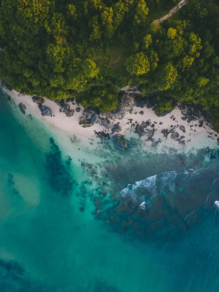 Aerial drone shot of tropical turquoise ocean waves and limestone cliffs along Bali coastline by Bali Assist Co