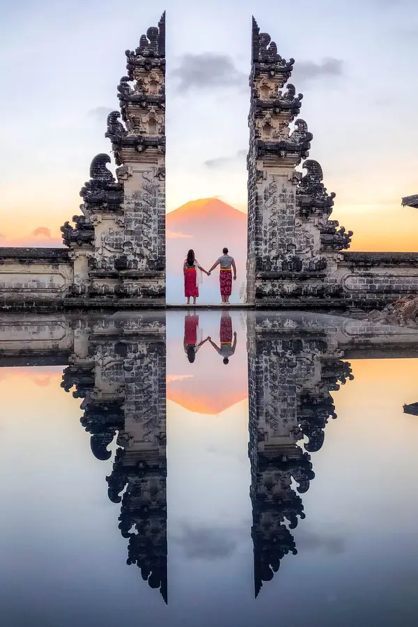 Couple holding hands at Lempuyang Temple Gate of Heaven with Mount Agung reflection for romantic Bali honeymoon organized by Bali Assist Co luxury tour