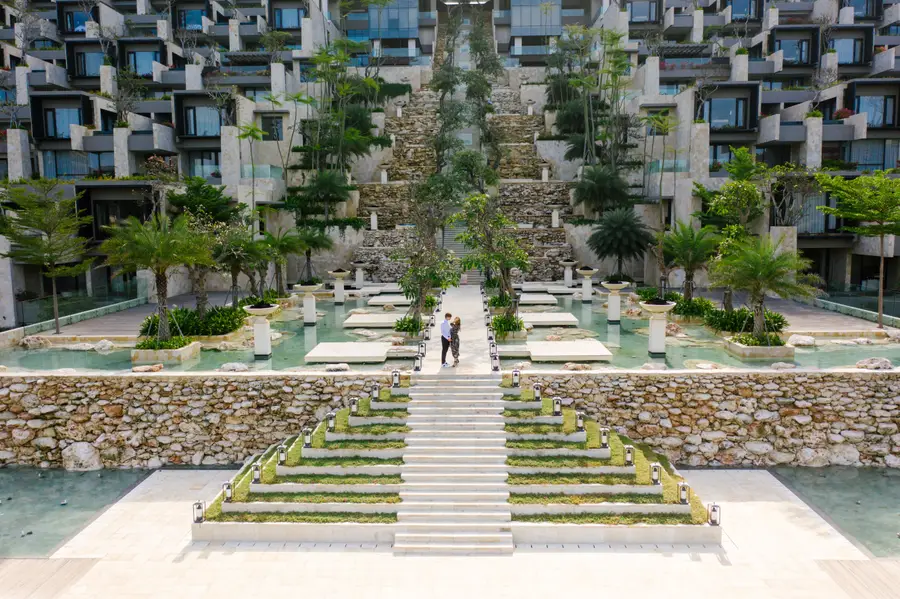 Couple standing at a modern luxury resort with grand stone stairs and water ponds in Bali by Bali Assist Co