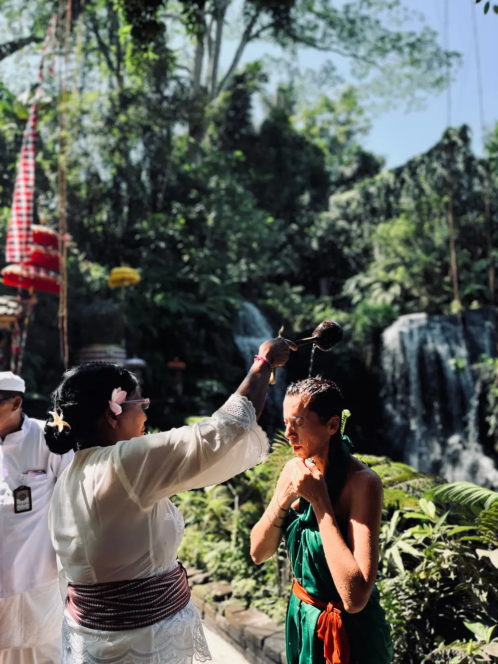 Balinese priest pouring holy water over a woman during Melukat cleansing ritual for The Discovery package by Bali Assist Co