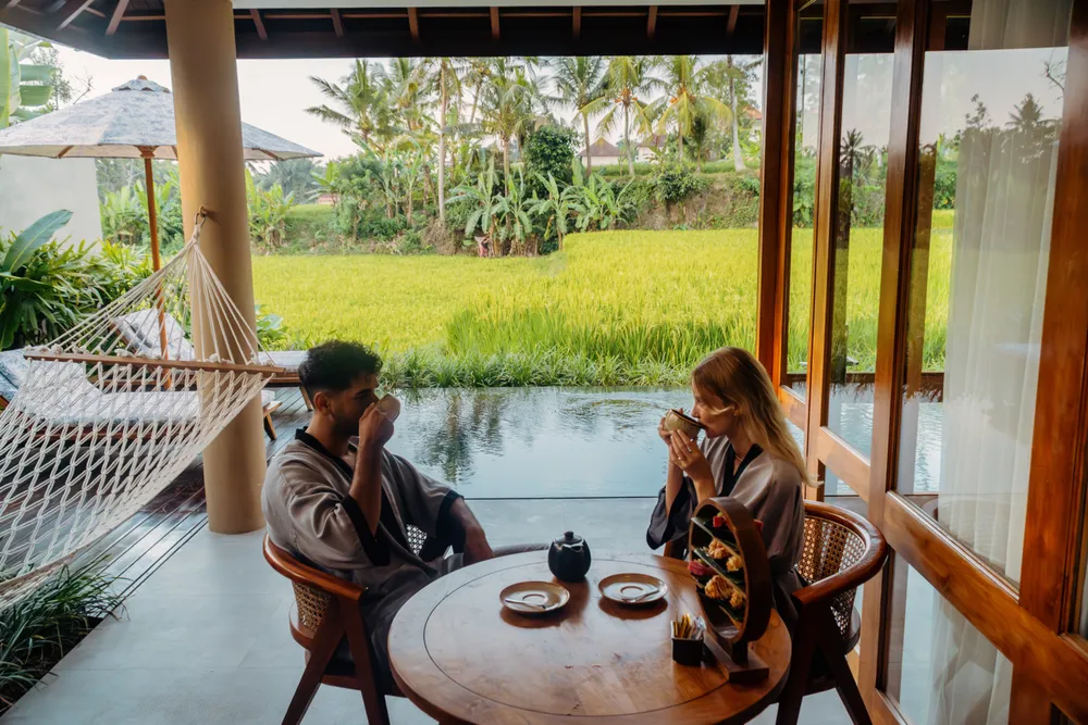 Couple enjoying tea overlooking lush green rice fields at Ubud resort for The Discovery Day 1 by Bali Assist Co