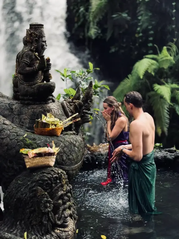 Couple praying during traditional Melukat water purification ceremony at waterfall for The Discovery Day 5 by Bali Assist Co