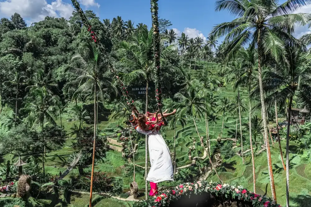 Woman riding high swing surrounded by coconut palms at Alas Harum Ubud for The Grand Escape Day 6 by Bali Assist Co