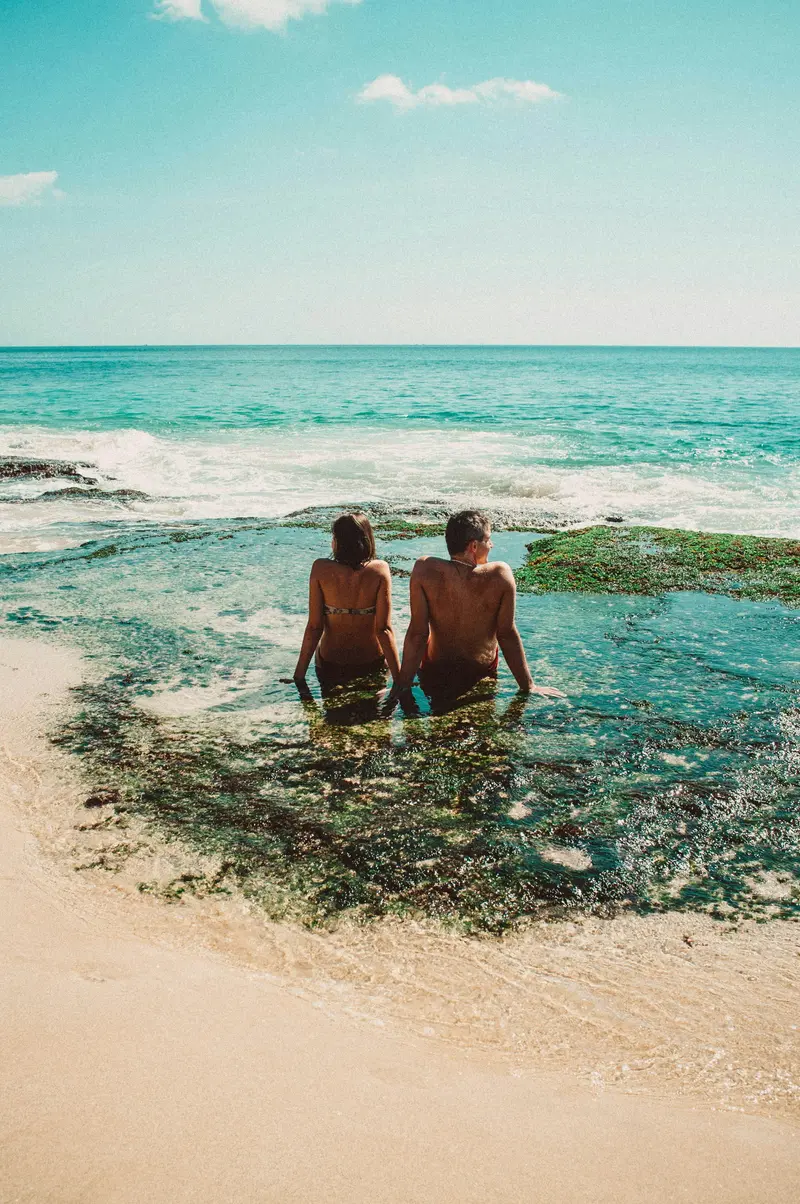 Couple relaxing on coastal cliff rocks overlooking clear turquoise ocean in Bali for The Grand Escape package by Bali Assist Co