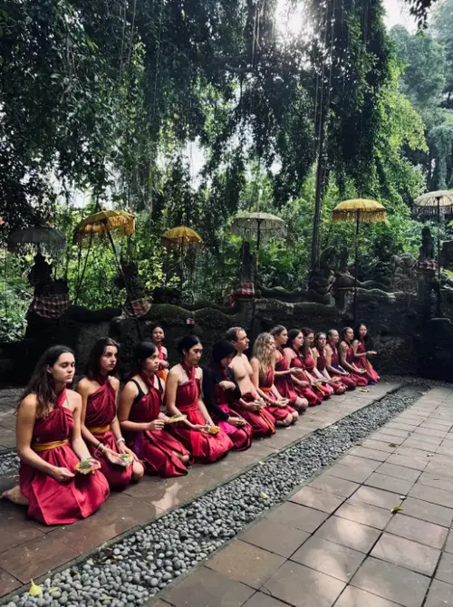 Group of participants wearing red sarongs praying in line during Melukat ritual by Bali Assist Co