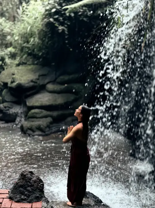 Woman standing in meditation under Taman Beji Waterfall during Melukat ceremony for The Grand Escape Day 8 by Bali Assist Co