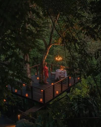 Couple having a romantic dinner at Kamandalu Ubud treehouse deck surrounded by jungle candles by Bali Assist Co
