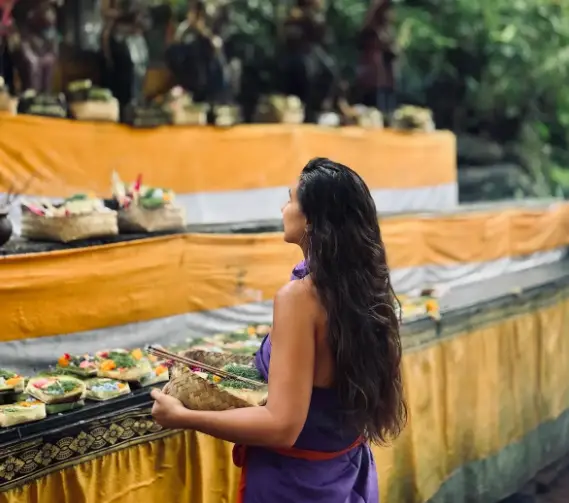 Woman carrying Canang Sari offerings during Melukat ceremony for The Indulgence package by Bali Assist Co