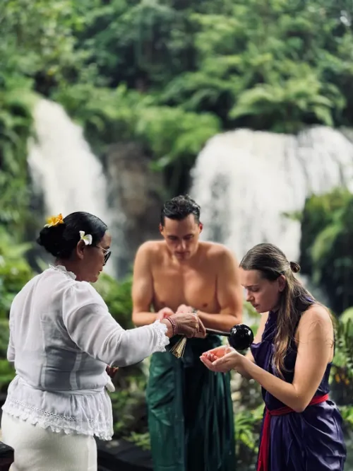 Balinese priest performing Melukat water cleansing ritual for a couple at Beji Waterfall by Bali Assist Co
