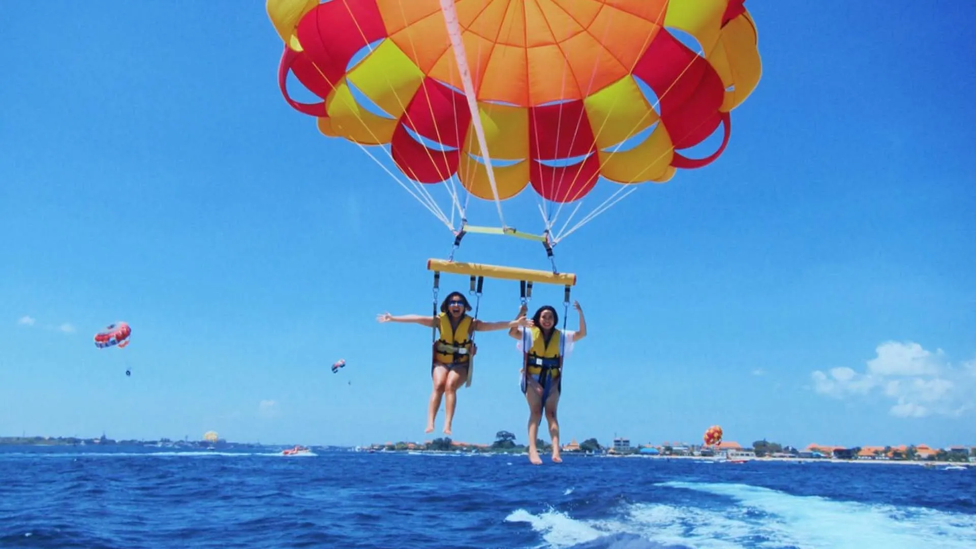Two women enjoying tandem parasailing watersport activity over Tanjung Benoa ocean for The Journey Day 6 by Bali Assist Co