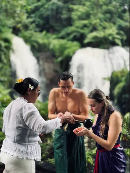 Priest pouring holy water on tourist during Melukat cleansing ritual at Taman Beji Waterfall for The Signature Journey Day 8 by Bali Assist Co