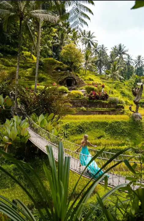 Woman walking on wooden suspension bridge surrounded by coconut palms at Alas Harum Ubud by Bali Assist Co