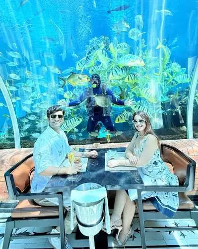 Scuba diver feeding tropical fish inside aquarium tunnel at Koral Restaurant Bali by Bali Assist Co
