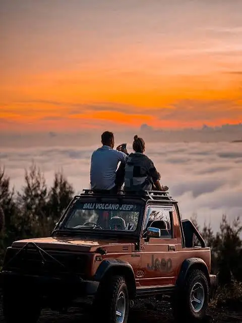 Couple sitting on 4WD jeep roof watching sunrise over sea of clouds at Mount Batur for The Ultimate Bali Journey Day 7 by Bali Assist Co