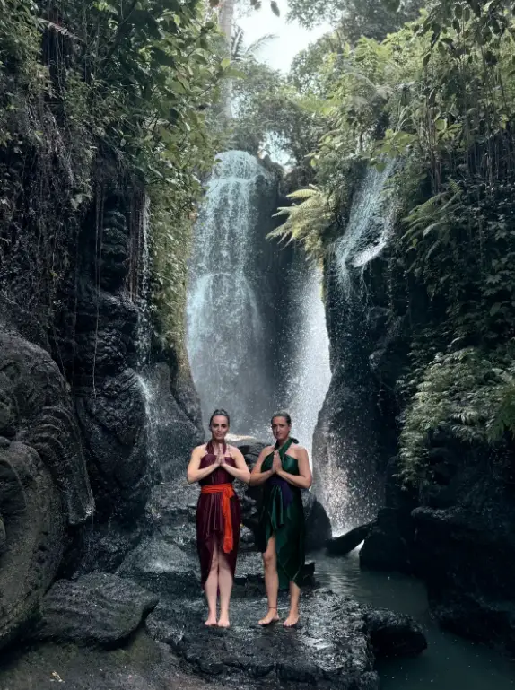 Couple standing together in front of cascading Taman Beji Waterfall after Melukat ritual in Ubud by Bali Assist Co