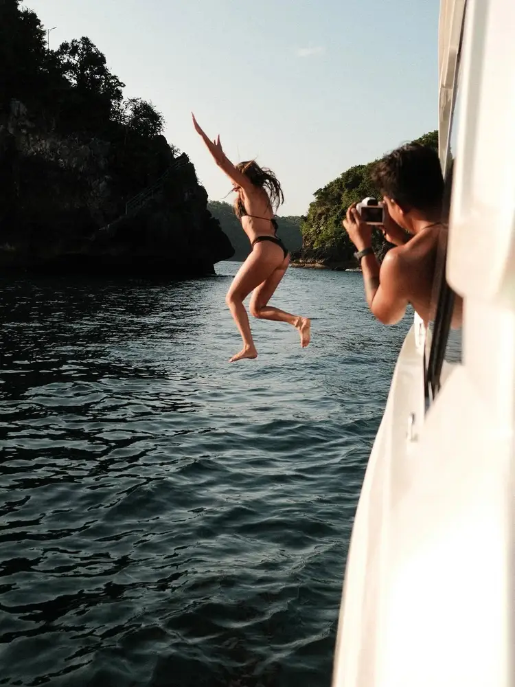 Woman jumping off luxury yacht into blue ocean water off Nusa Penida coast by Bali Assist Co