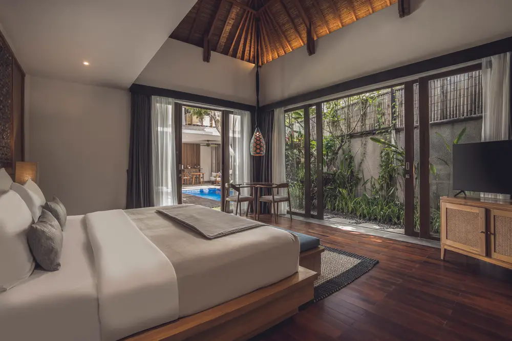 Spacious Balinese high-ceiling villa bedroom with wooden floor and private pool view by Bali Assist Co