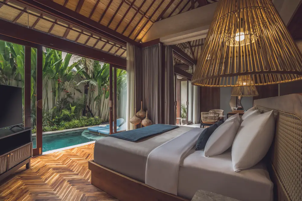 Luxury villa bedroom with high wooden ceiling, bamboo pendant light, and private pool garden access in Bali by Bali Assist Co